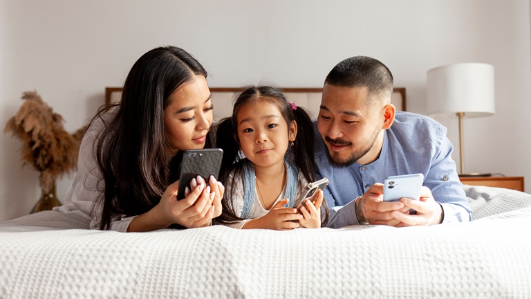 a young family holding smartphones on the bed