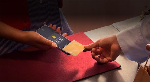 A hand taps a credit card to an iPhone to complete a payment